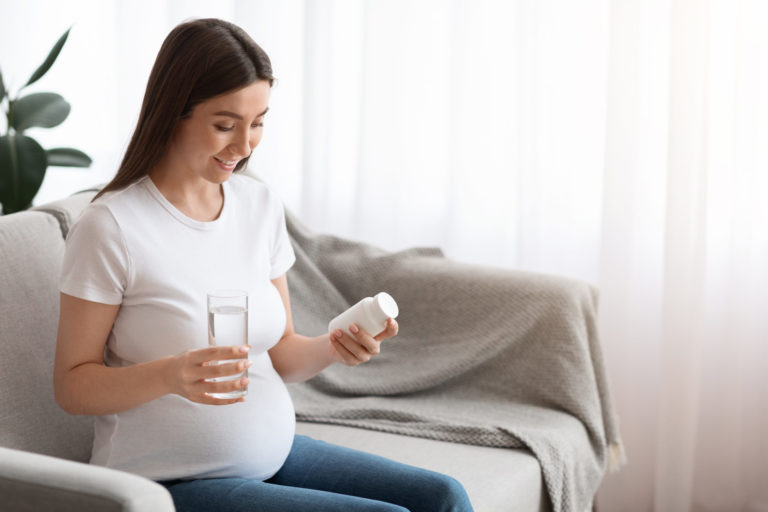 Supplements During Pregnancy. Pregnant Woman Holding Jar With Vitamins And Water Glass